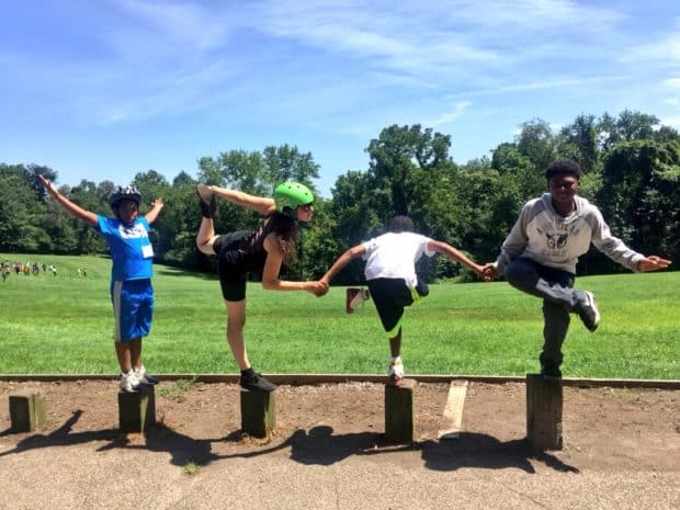 Three young men and their teacher stand in a line on top of longs, each balancing on one foot and making poses with their arms. Many are holding hands and one throws his arms up in triumph. This picture is also adorable. 