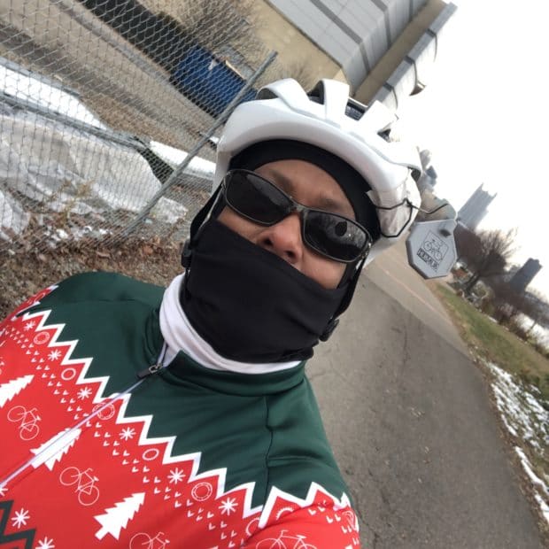 Robin Woods wears a buff and hat with a helmet, and a holiday sweater