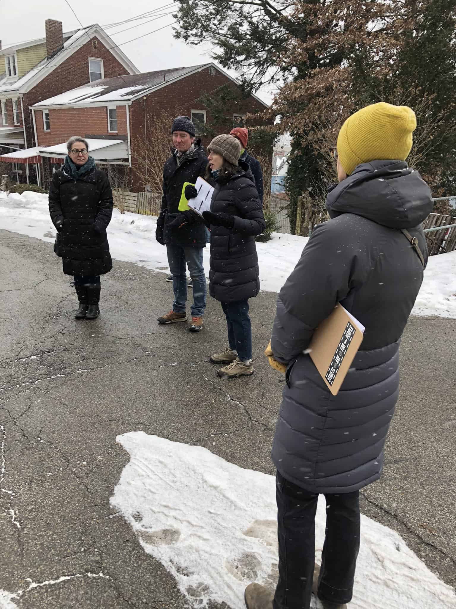 Woman speaks to a group of five people on a snow-covered road. 