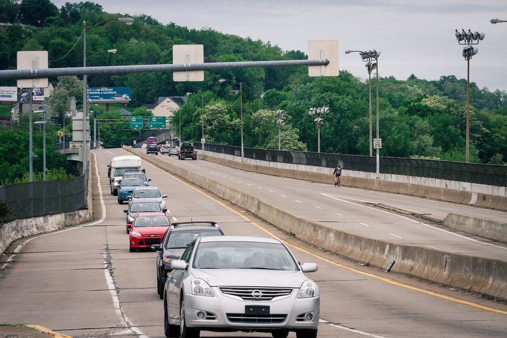 Image shows the Bloomfield Bridge with a line of cars and a bicyclist among them