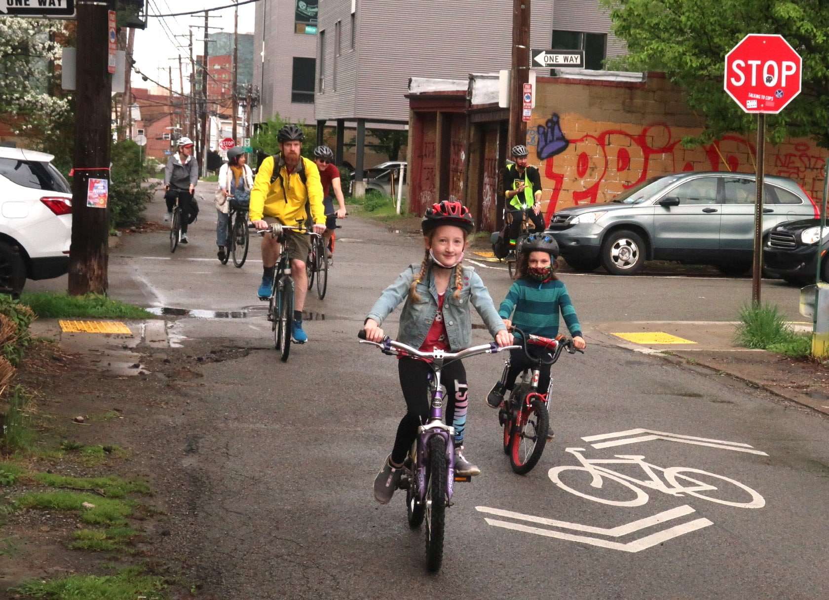 Photography of a group of children and  adults biking down a neighborway. 