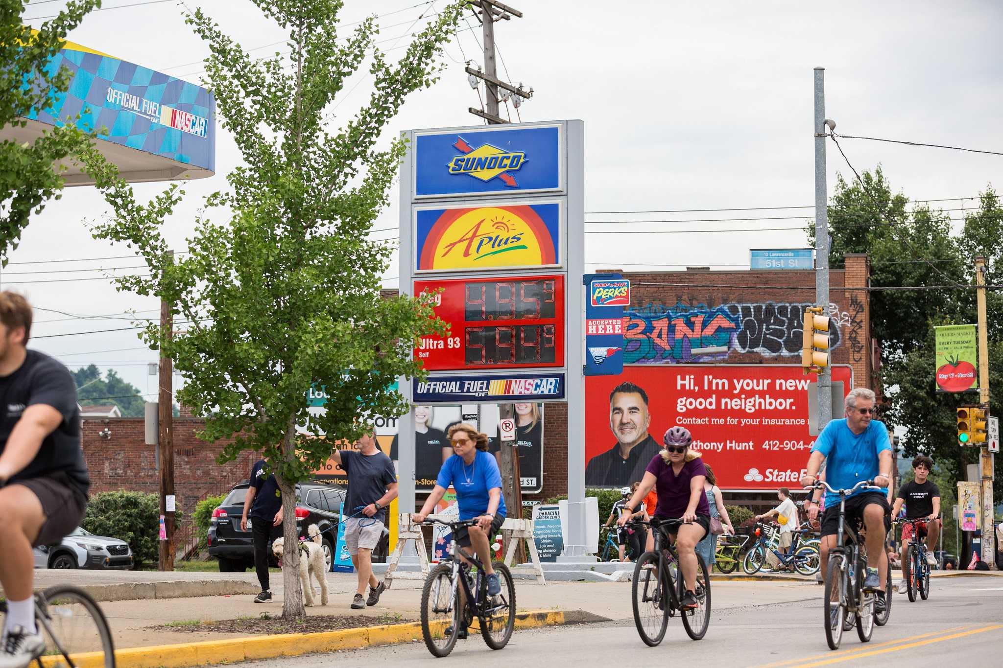 People on bikes ride in front of a Sunoco gas station sign showing $4.95 per gallon prices. 