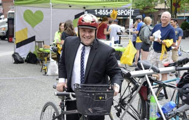 man standing with bicycle facing the camera wearing red helmet, smiling big