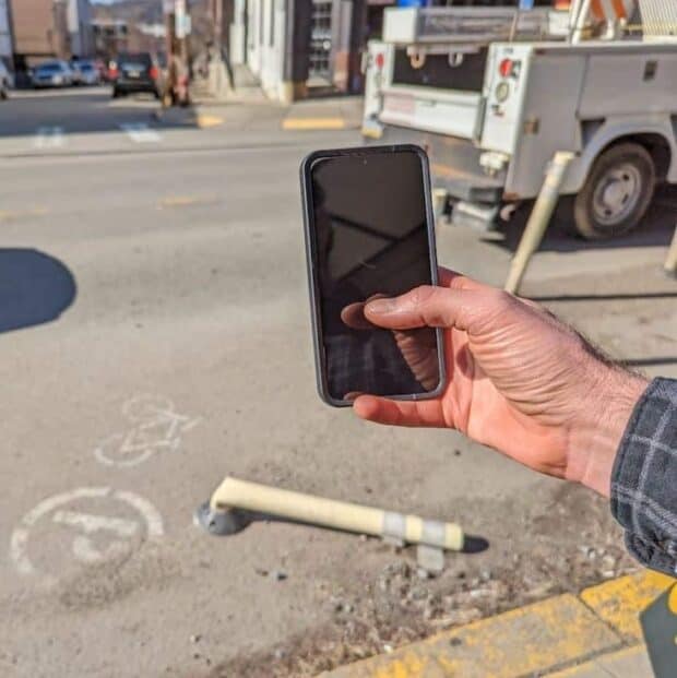 Picture of a hand holding a phone and taking a picture of a broken bollard.