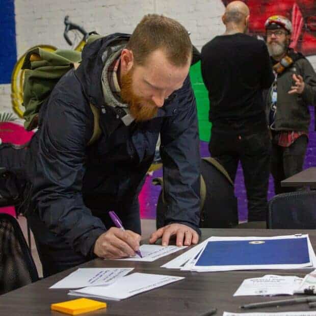 Picture of someone with a bike helmet on their backpacking leaning over a desk and writing a letter.