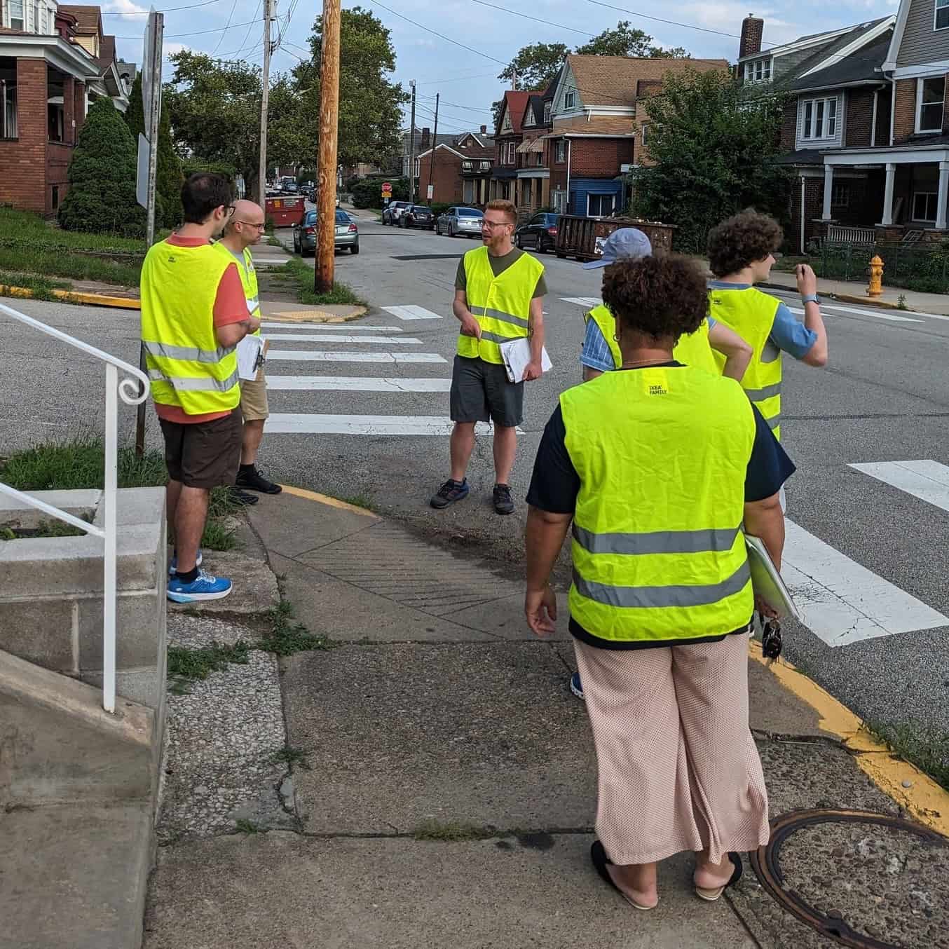 Picture of people wearing yellow high visibility vests gathered around a broken sidewalk.