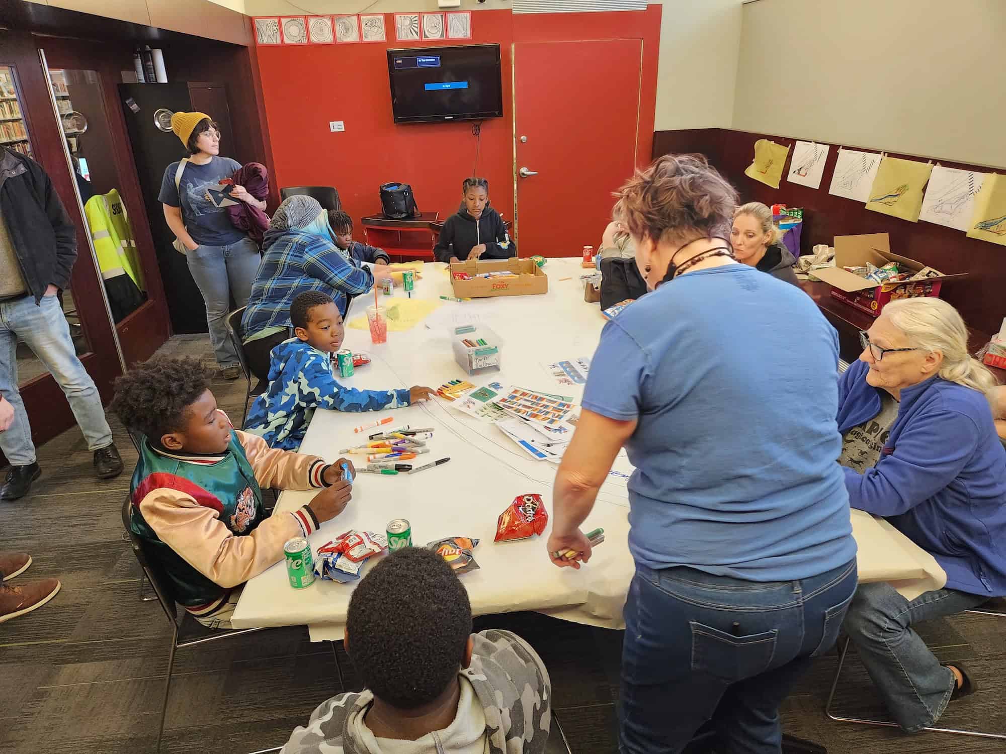 Image of adults and children surrounding a table with drawing implements inside the library