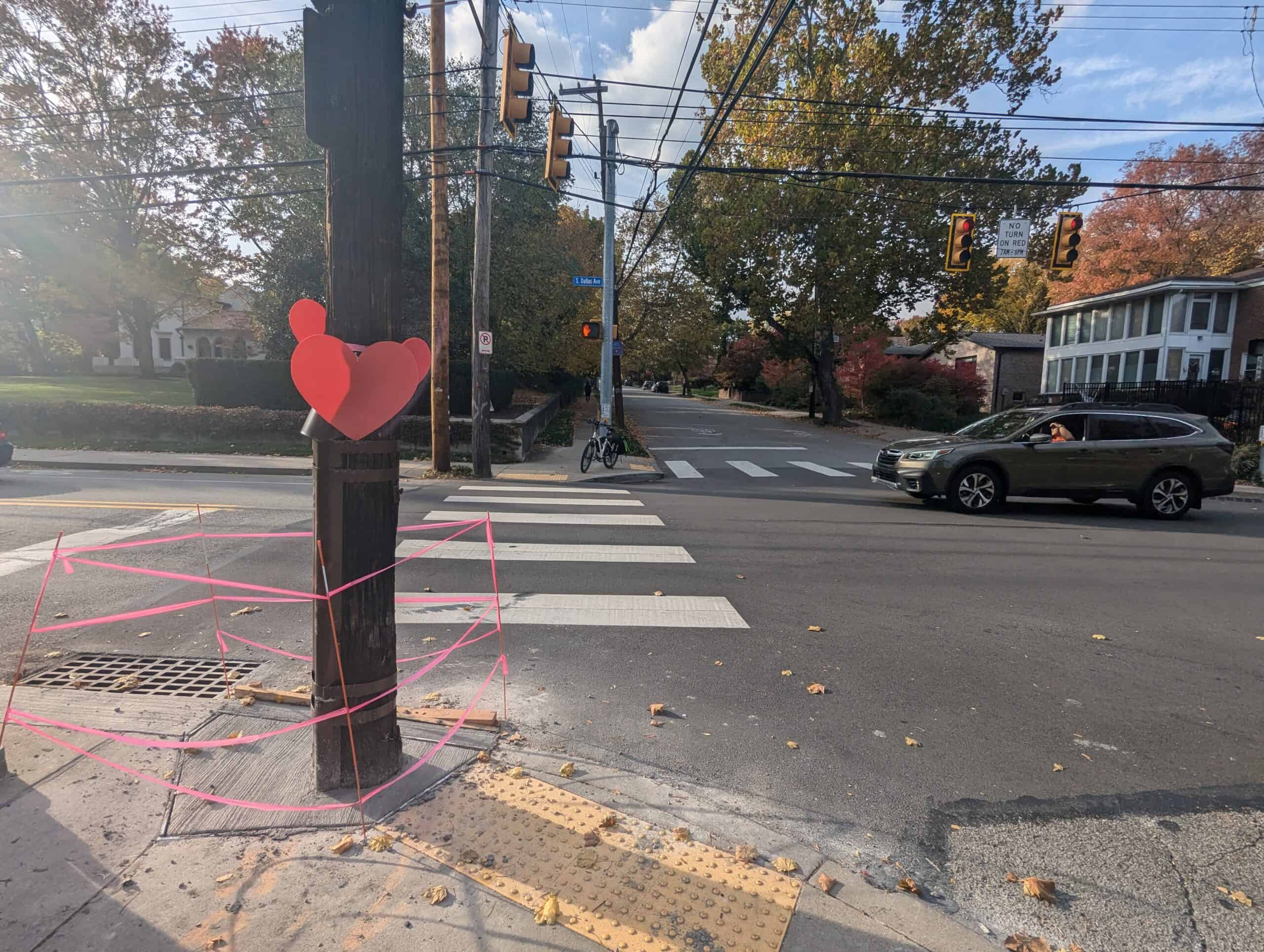 A picture of the crosswalk and curb cuts at the intersection at Dallas Ave and Reynolds St. A utility pole has handmade hearts stapled onto it where Vira was killed.