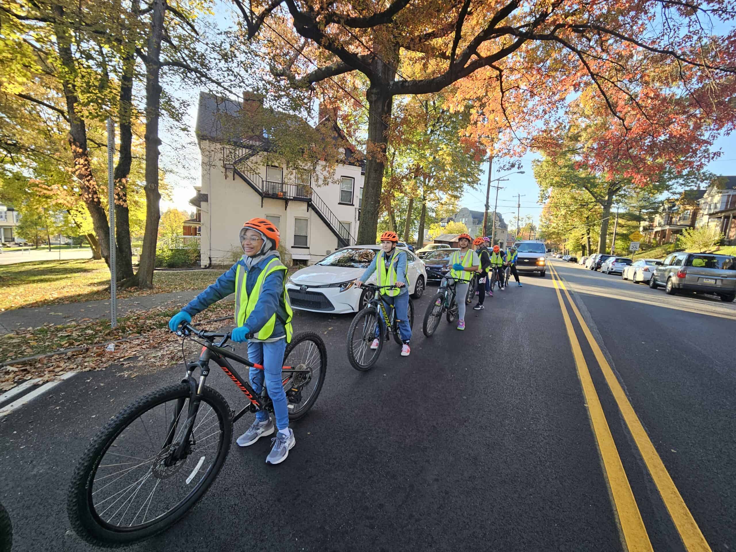 A line of ten middle school students on bikes is smiling while stopping at an intersection during their bike ride. 