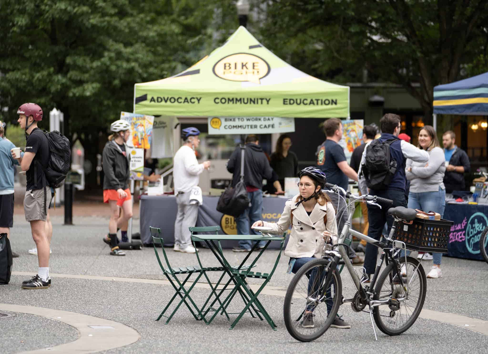 An image of Market Square during the 2024 Bike to Work Day event, showing a woman sitting at a table next to her bicycle.