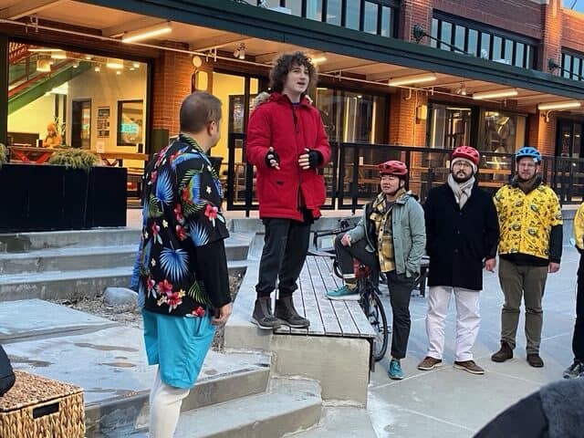 A person in a red jacket speaks with others wearing tropical shirts.