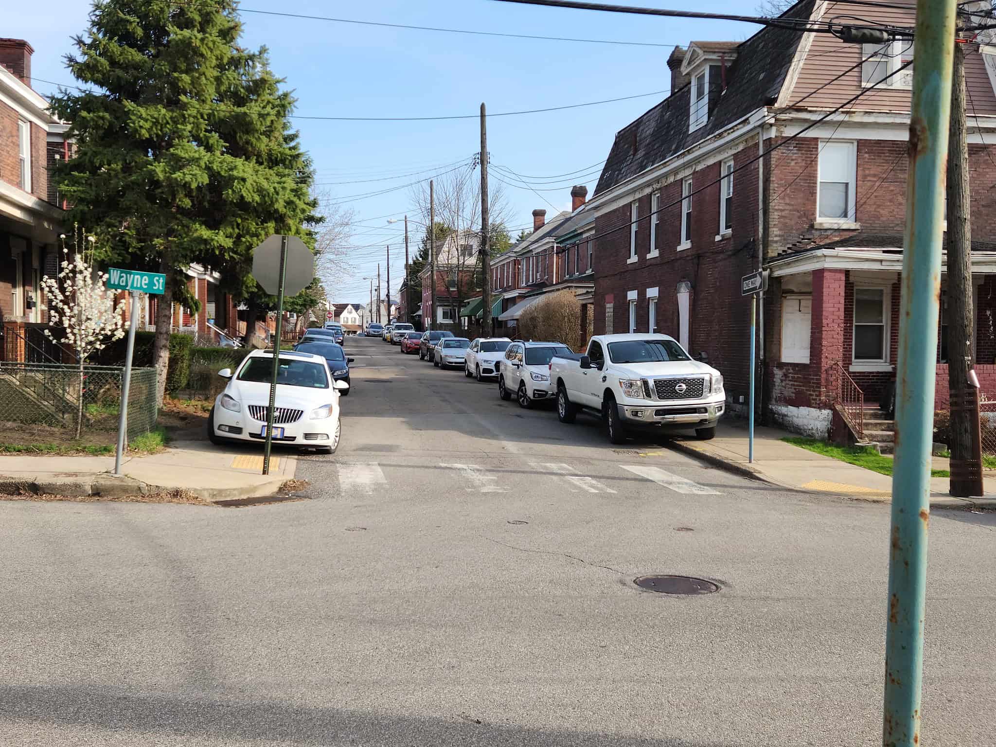 Photo of cars parked fully on the sidewalks on both sides of a street, blocking pedestrian access.