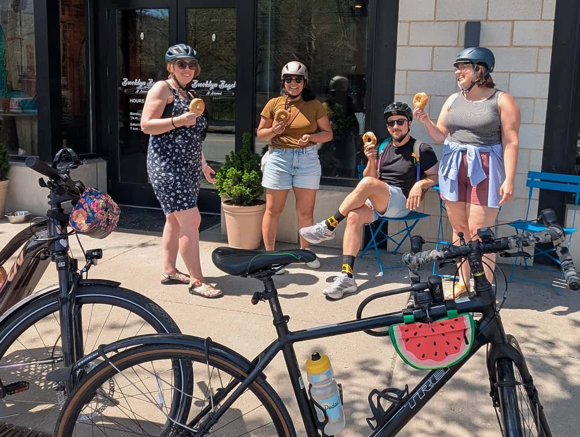 Four of BikePGH's staff smiling and enjoying bagels together with their bikes