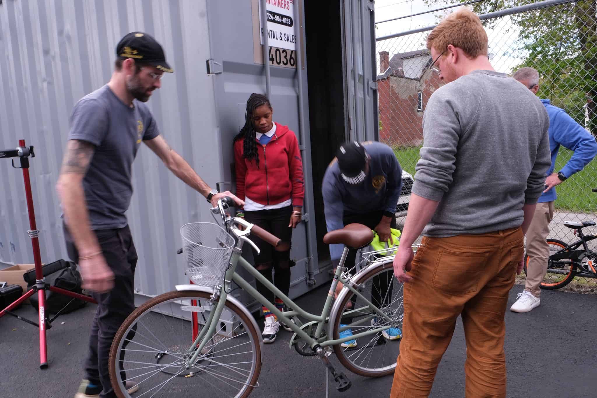BikePGH staff tune-up a bike while a young person watches.
