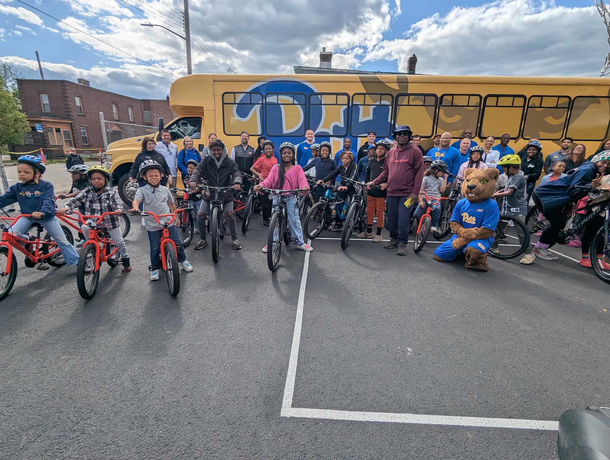 Youth at The Promise Center pose with their new bikes in front of the Pitt Athletics shuttle bus.