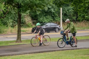 BikePGH staff member rides a bike alongside a student at The Bud Harris Cycling Track. 