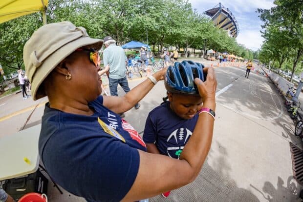 A BikePGH staff person places a bike helmet on a child
