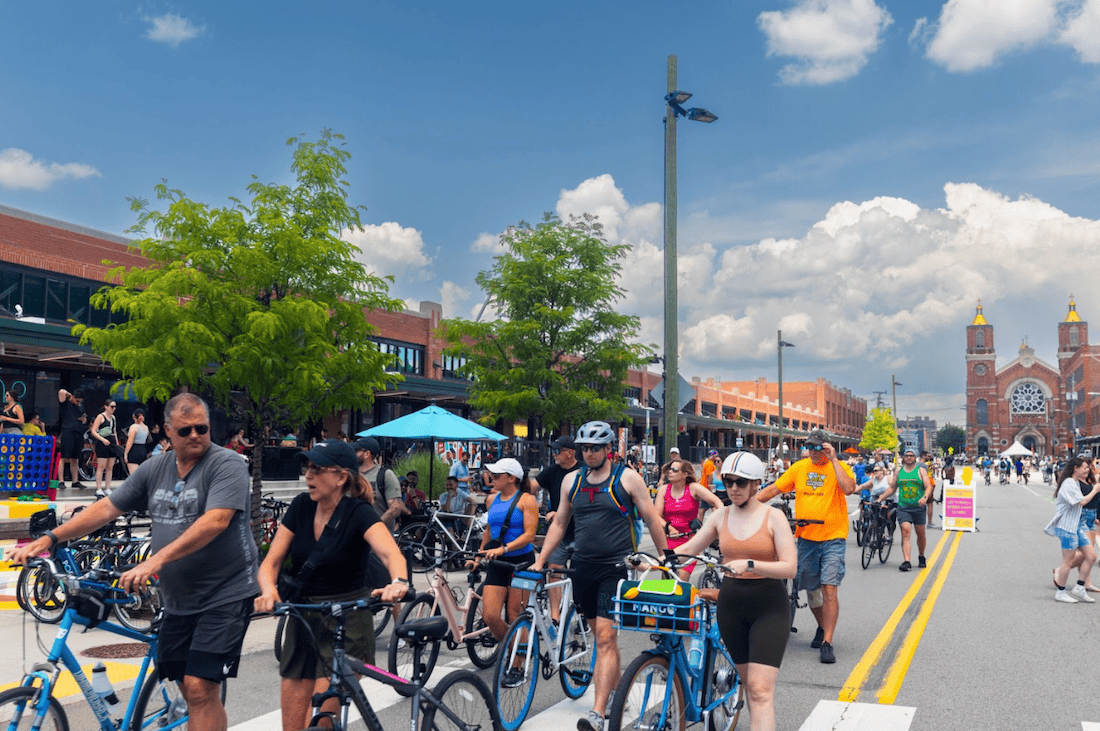 OpenStreetsPGH participants walk their bikes outside The Strip District Terminal on a sunny day with a smattering of clouds