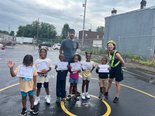 Six younger students post with their instructors while they hold their safe cycling awards.