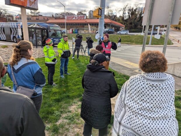 A person in a pink hi-visability vest speaks to an audience through a megaphone.