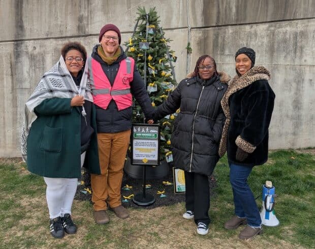 People gather around a memorial tree. They are smiling and holding hands.