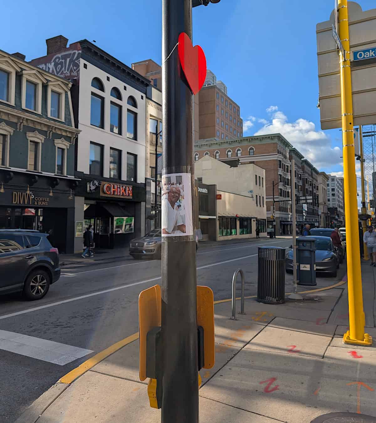 A utility pole with a heart on it that says "bobby paige" with the image of an older smiling Black man on printer paper taped below.