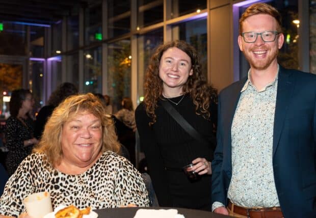 photo shows three people smiling at an indoor event - Seth and Julie from BikePGH with Bernadette, a Brookline resident and friend of the org.