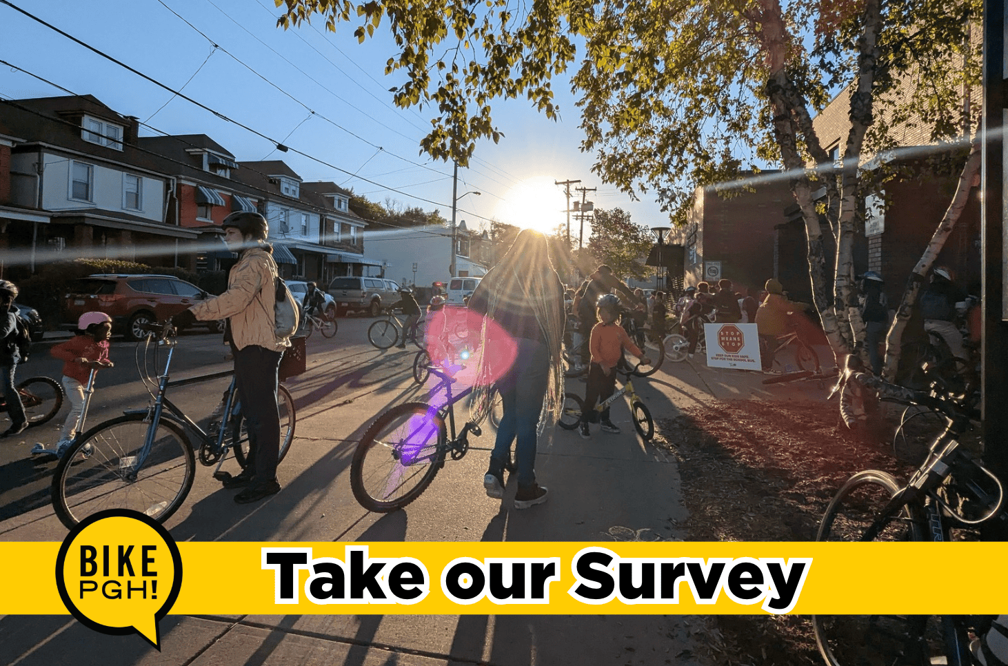 The words "Take Our Survey" over a photo of kids riding bikes outside of a school on a sunny morning. 