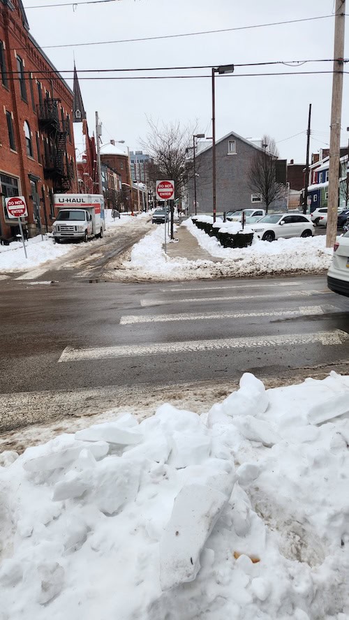 A curb cut to a crosswalk is fully swallowed by snow.