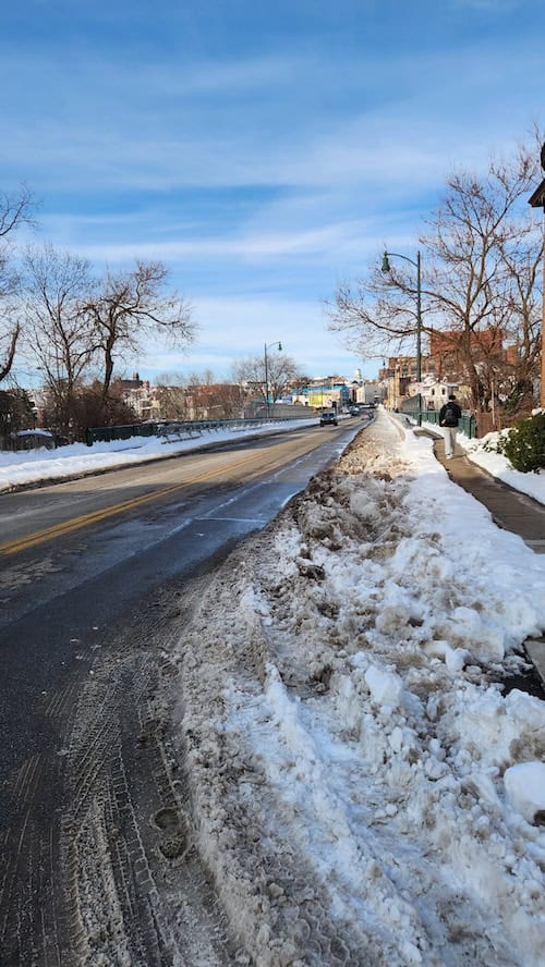 Several inches of dirty, heavy, icy snow completely covers a bike lane, while the road remains open and plowed clean. 