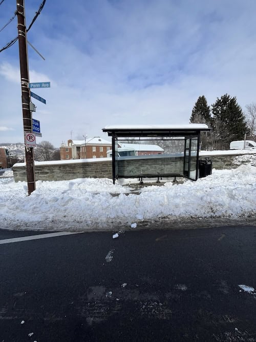 A bus stop covered in snow, with no clear pathway from it to the street.