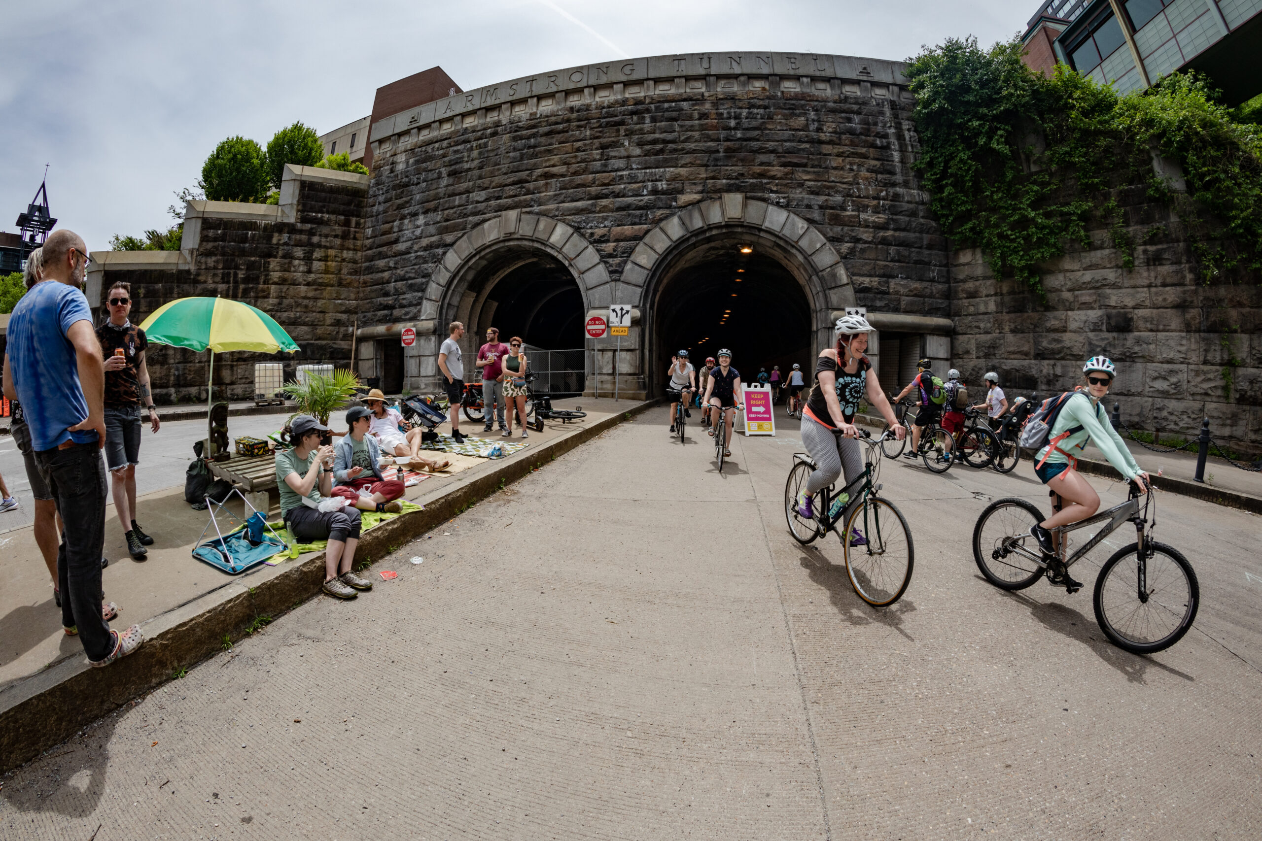 An image of car-free Armstrong Tunnel., with about 20 or so bikers smiling and riding through