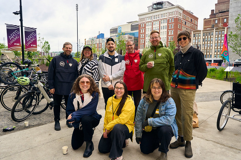 BikePGH staff group photo at Bike to Work Day - Smiling in their rain gear with coffee at Arts Landing in Downtown