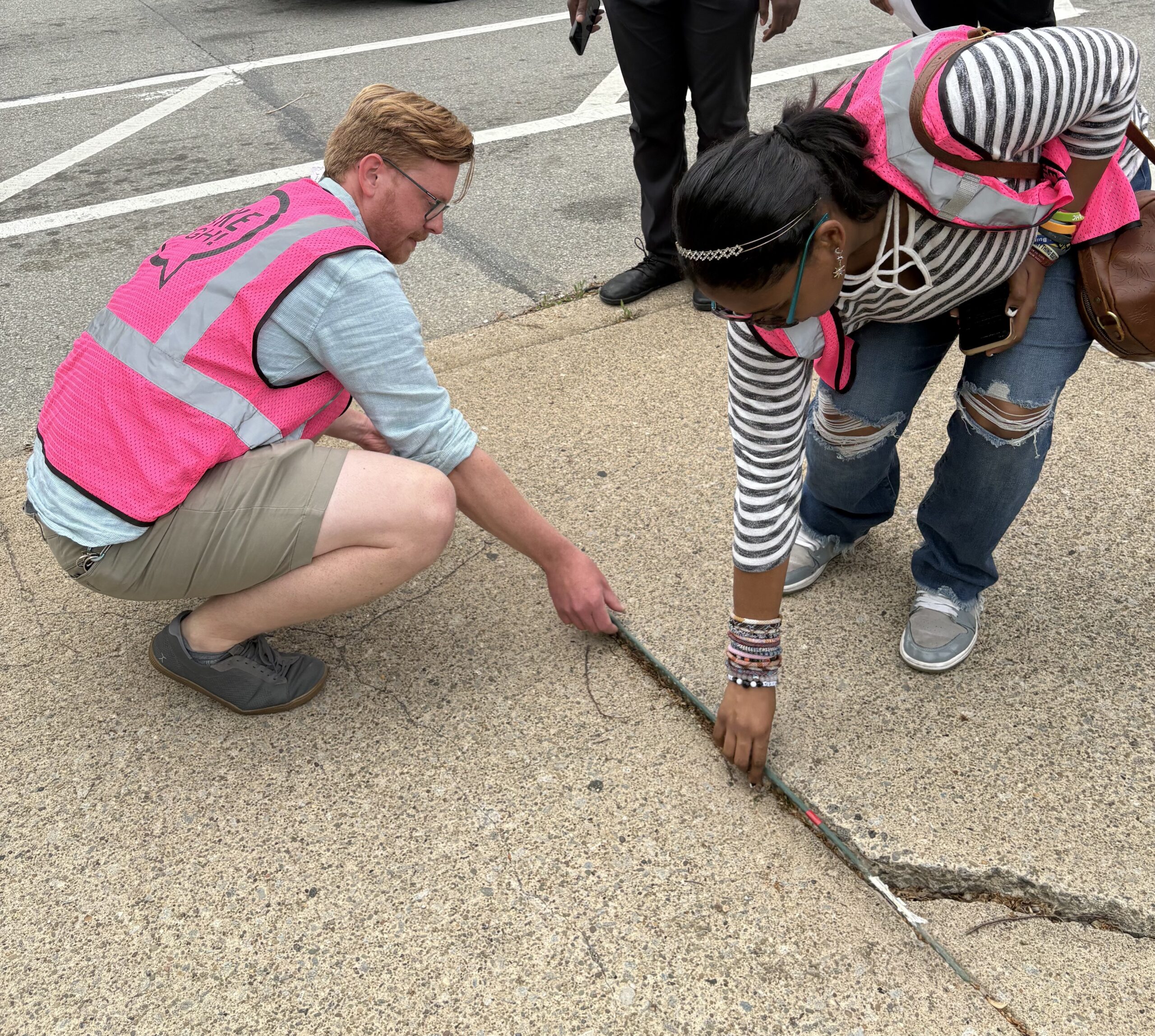 A walk audit participant using a four-foot tomato stake to measure sidewalk width. 