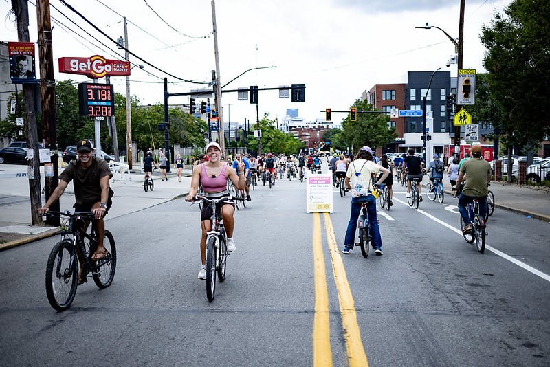 a photo of a car-free Butler Street, right outside of the Get Go gas station, with gas prices looming in the background. The people on bikes are smiling and riding