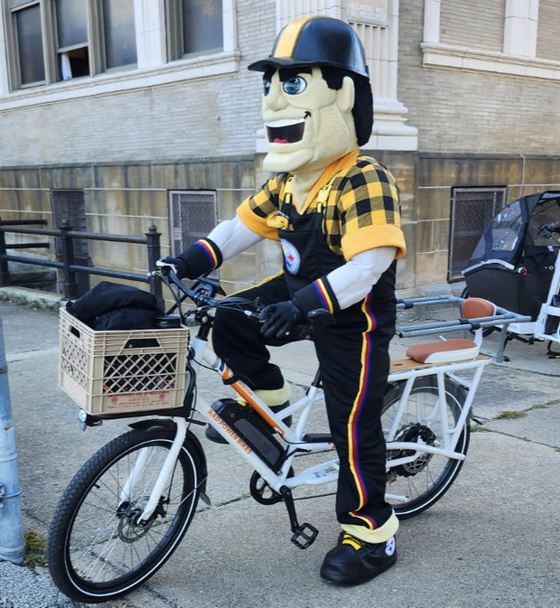 Steely McBean, Steelers mascot, on a bicycle at Pittsburgh Montessori school.